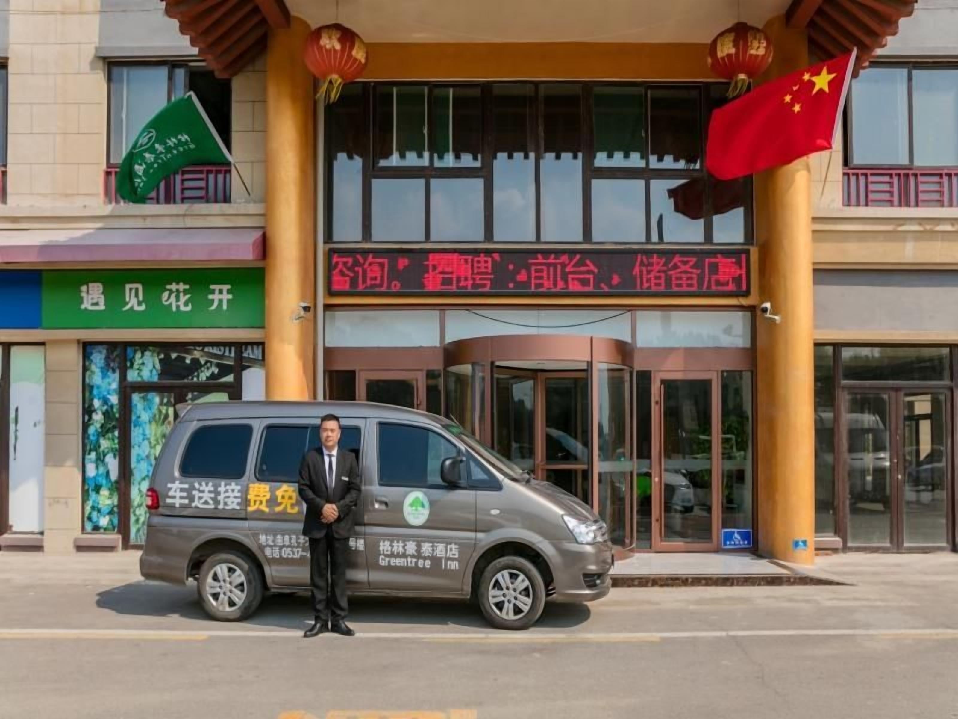 A man standing in front of a building with a sign that reads 'Car Delivery Free Zone.'