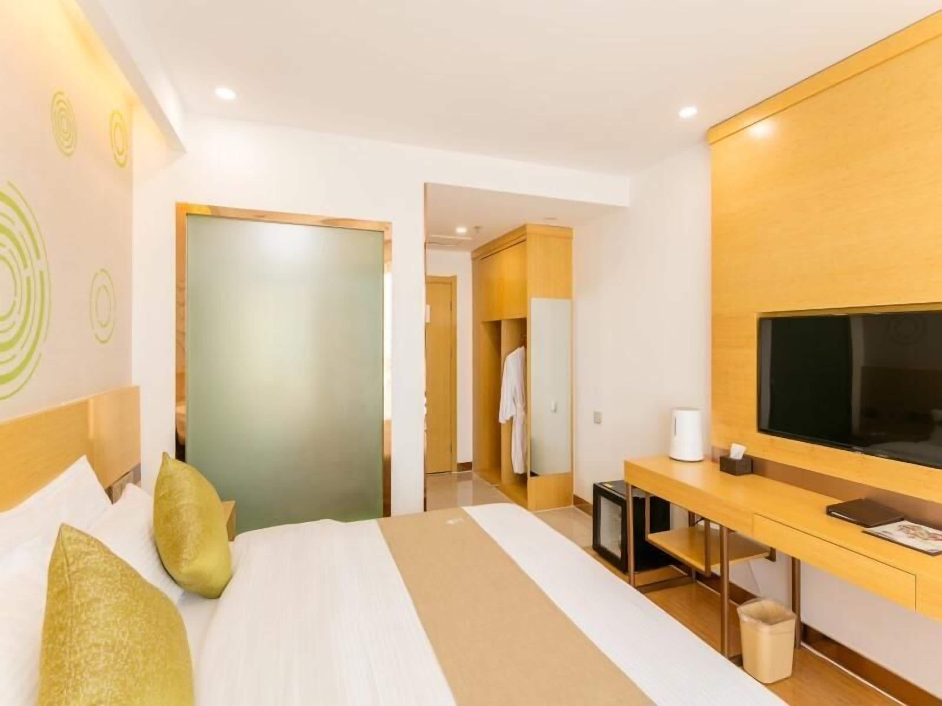 Ein Hotelzimmer mit einem Bett, einem Schreibtisch mit Computer, einem Fernseher und einem Kleiderschrank.