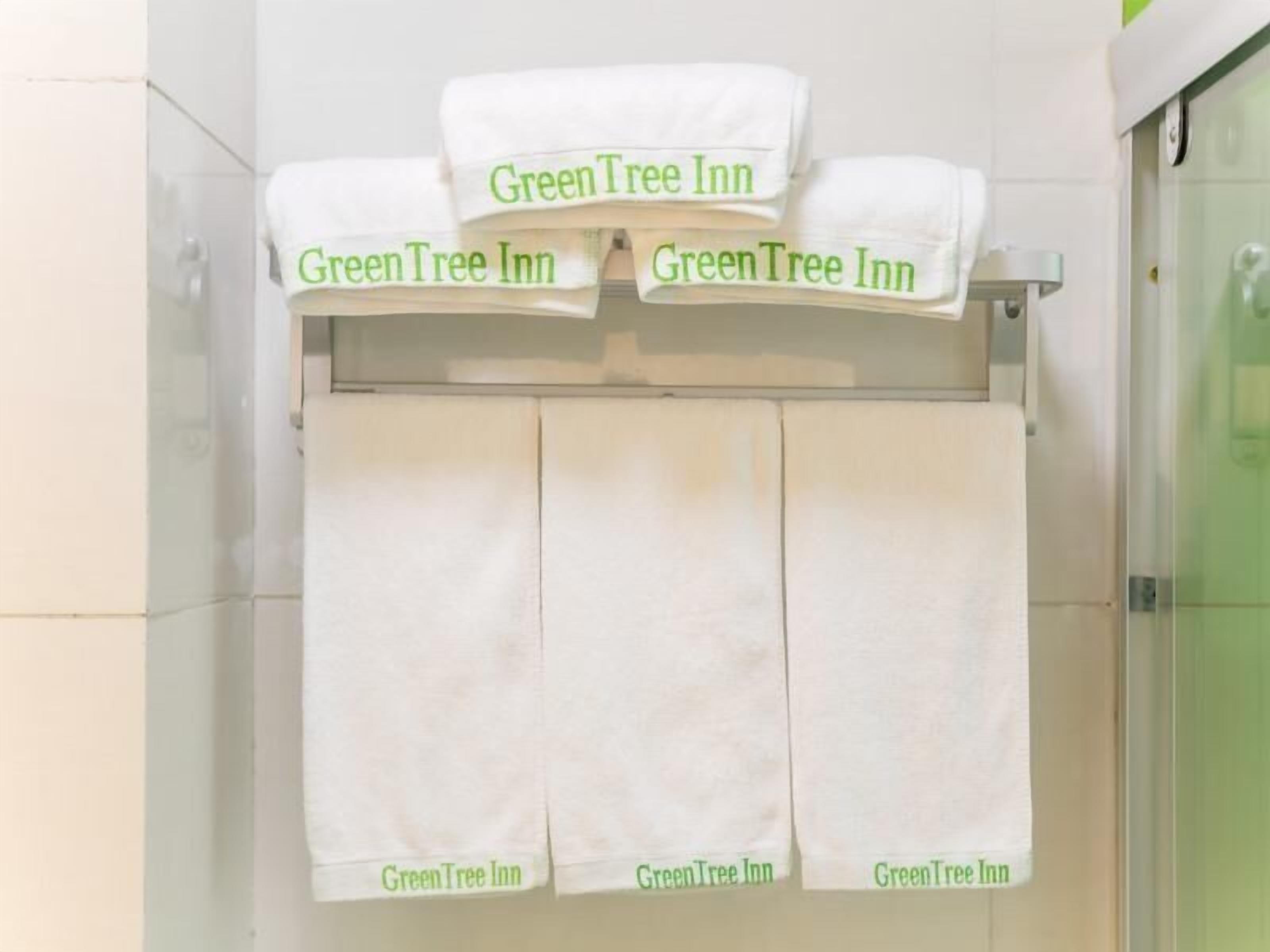 A bathroom with three white towels hanging on a rack, each labeled "GreenTree Inn".