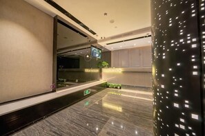 Un moderno vestíbulo de hotel con una recepción, una pantalla digital y una planta decorativa.