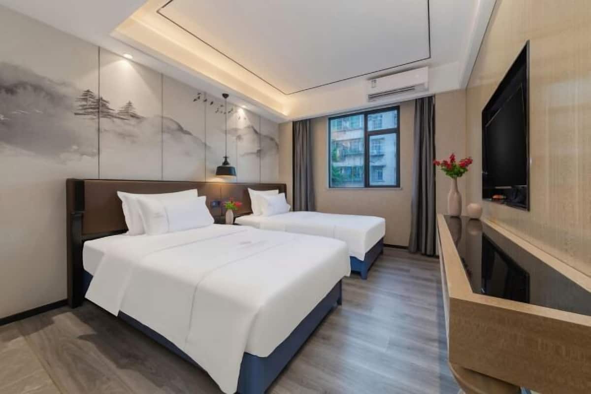 Ein Hotelzimmer mit zwei Betten, einem Fernseher, einem Schreibtisch und einem großen Fenster.