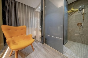 A modern bathroom with a glass shower enclosure, a yellow chair, and a glass partition.