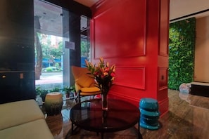 A lobby with a red wall, a yellow chair, a round table with a vase of flowers, and a green wall with plants. - Shangyuan Chain Hotel Guangzhou Railway Station (Guangzhou)