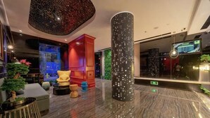Un vestíbulo moderno con techo alto, una columna central, zona de estar y una pantalla digital.