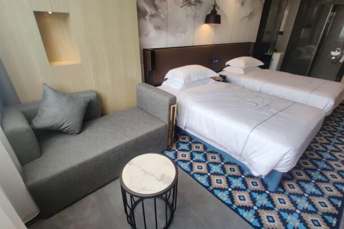 A hotel room with two beds, a sofa, a small round table, and a patterned carpet.