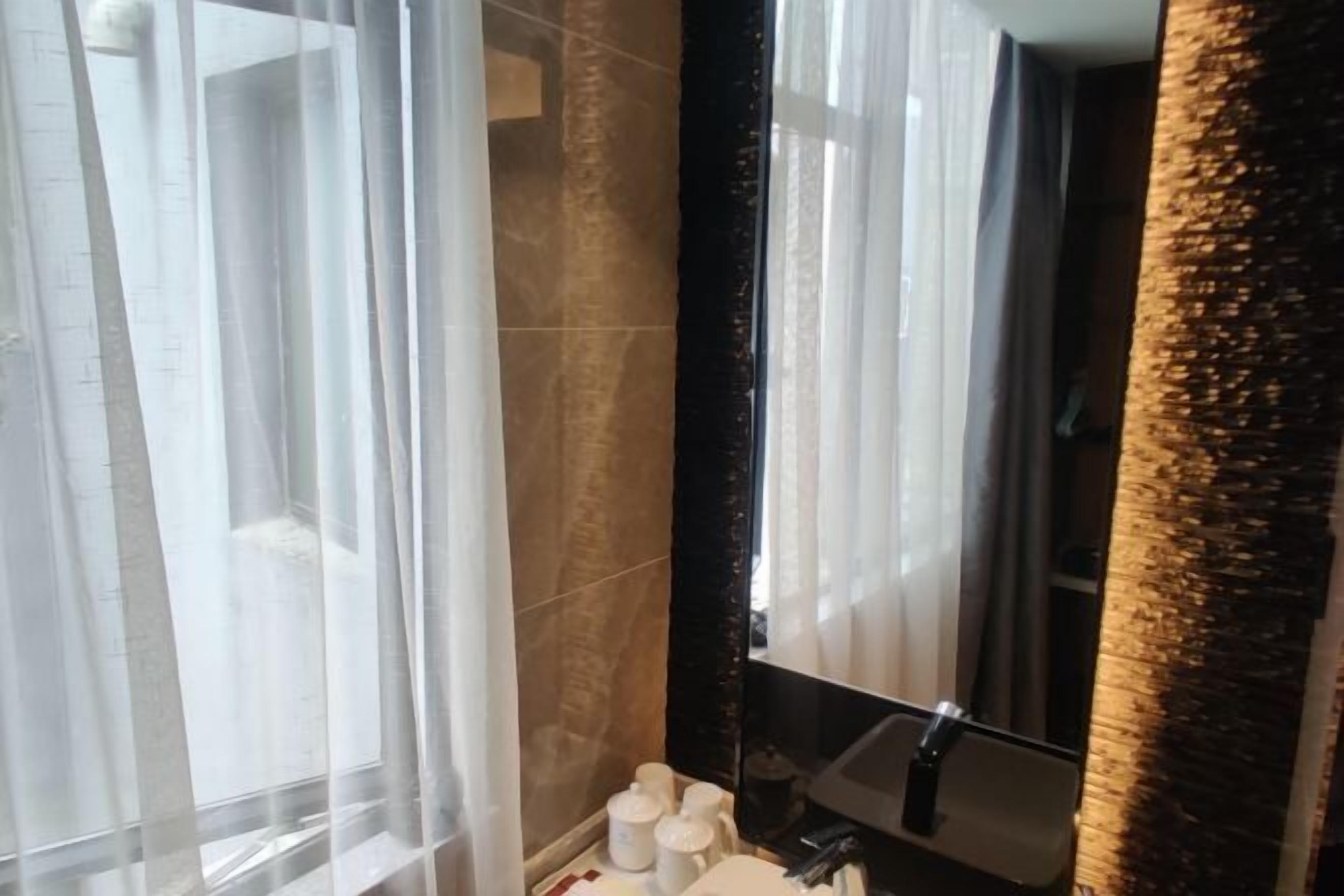 A bathroom with a large mirror, a sink, and a window with sheer curtains.