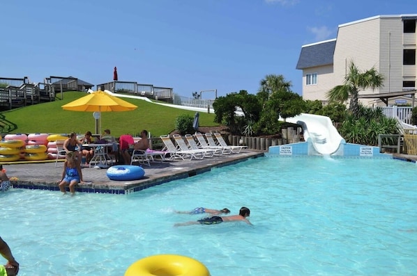 Relax by the pool surrounded by lounge chairs and umbrellas, with a restroom nearby.