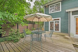 A wooden deck with a round table and chairs, an umbrella, and a house in the background. - Upscale Family Retreat w/ Fire Pit, Walk to Beach! (Union Pier)