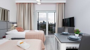 A modern hotel room with two beds, a dining area, a TV, and a city view.