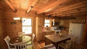 A wooden cabin interior with a dining area, kitchen, and a large window. - Gorgeous, tree top views from this cabin (Stanton)