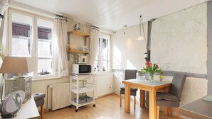 Une pièce bien éclairée, avec une table à manger, des chaises, un four à micro-ondes, un radiateur et une fenêtre avec des rideaux.