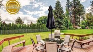 An outdoor patio with a table and chairs, a grill, and a wooden deck.