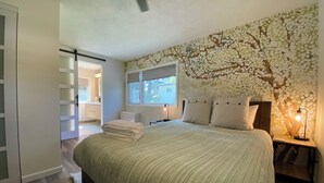 A bedroom with a bed, a nightstand, a window, and a wall with a tree mural.