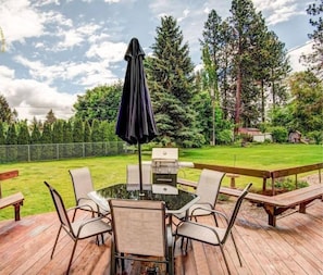 Een terras buiten met een tafel, stoelen, een barbecue en een houten vlonder.