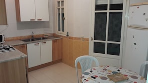 A compact kitchen with white cabinets, a sink, a stove, and a refrigerator. There's a window with a view of the outside, and a table with a patterned tablecloth.