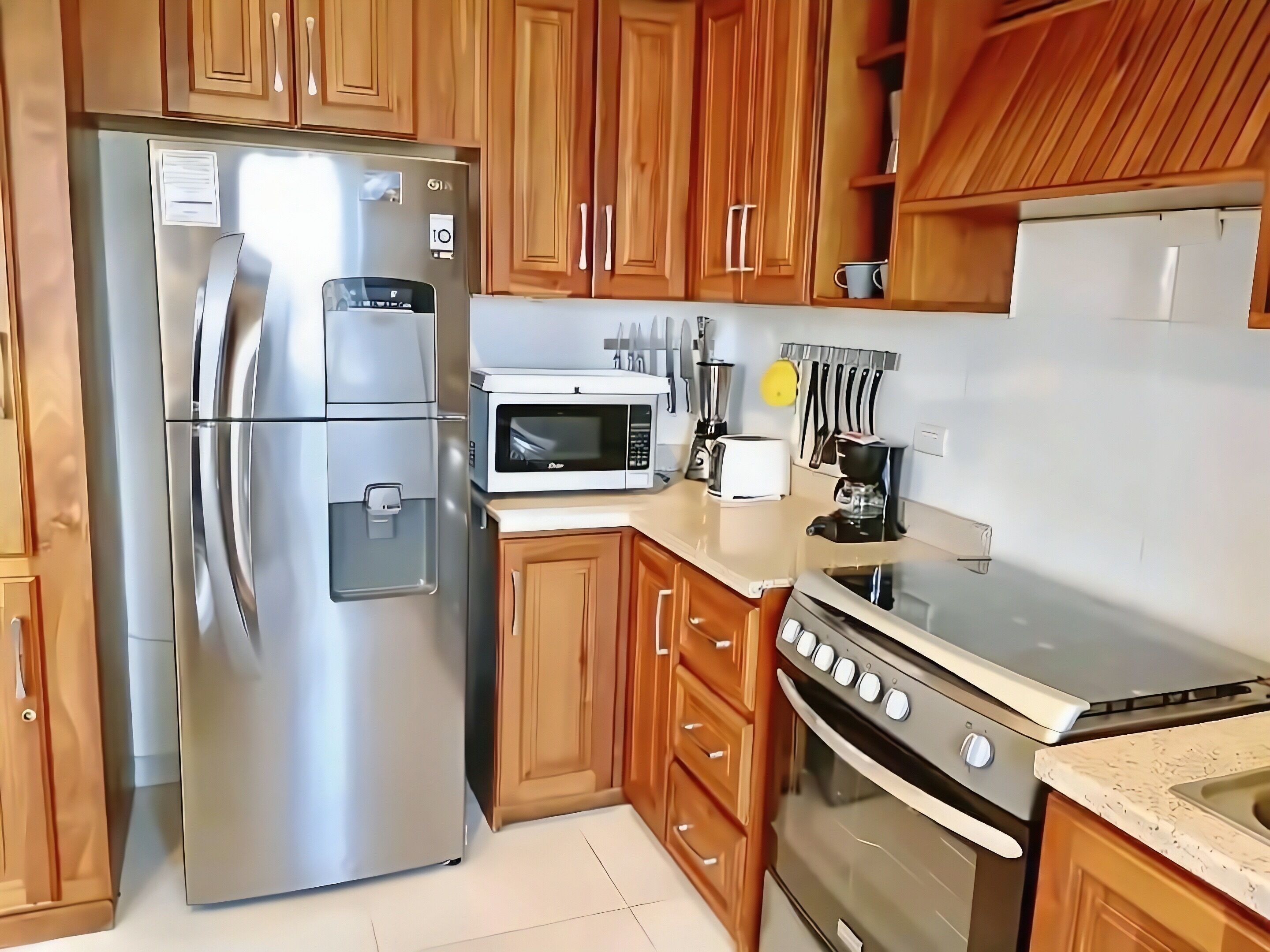 A kitchen with wooden cabinets, a stainless steel refrigerator, a microwave, a toaster, and an oven.