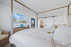 Un dormitorio con una cama grande, una mesita de noche de madera, un cuadro en la pared y una puerta que da a otra habitación.