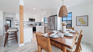 Una cocina moderna con gabinetes blancos, electrodomésticos de acero inoxidable y una mesa de comedor de madera con sillas.
