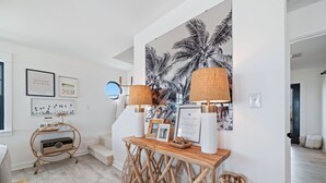Una sala de estar moderna con una consola de madera, una gran obra de arte con estampado de palmera tropical y una escalera que conduce a otro nivel.