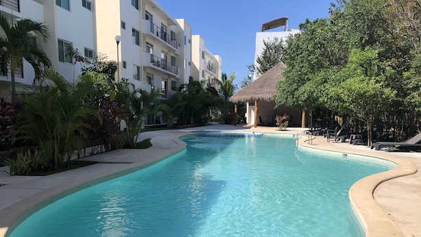 A swimming pool with a curved edge, surrounded by palm trees and a building with balconies. - Wonderful Caribbean !!! (Playa del Carmen)