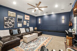 A room with a dark blue wall, a ceiling fan, a bench, a leather sofa, a patterned rug, and a guitar. - Private heated pool/hot tub, pickleball mini golf. 9 Bdrms. 4 bath. EV charger. (La Verkin)