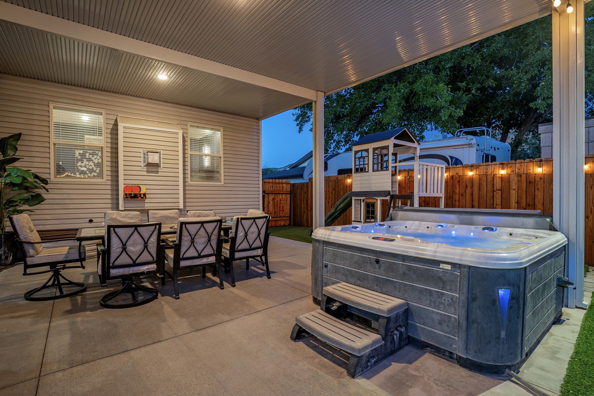 An outdoor patio with a hot tub, seating area, and a covered section with windows.