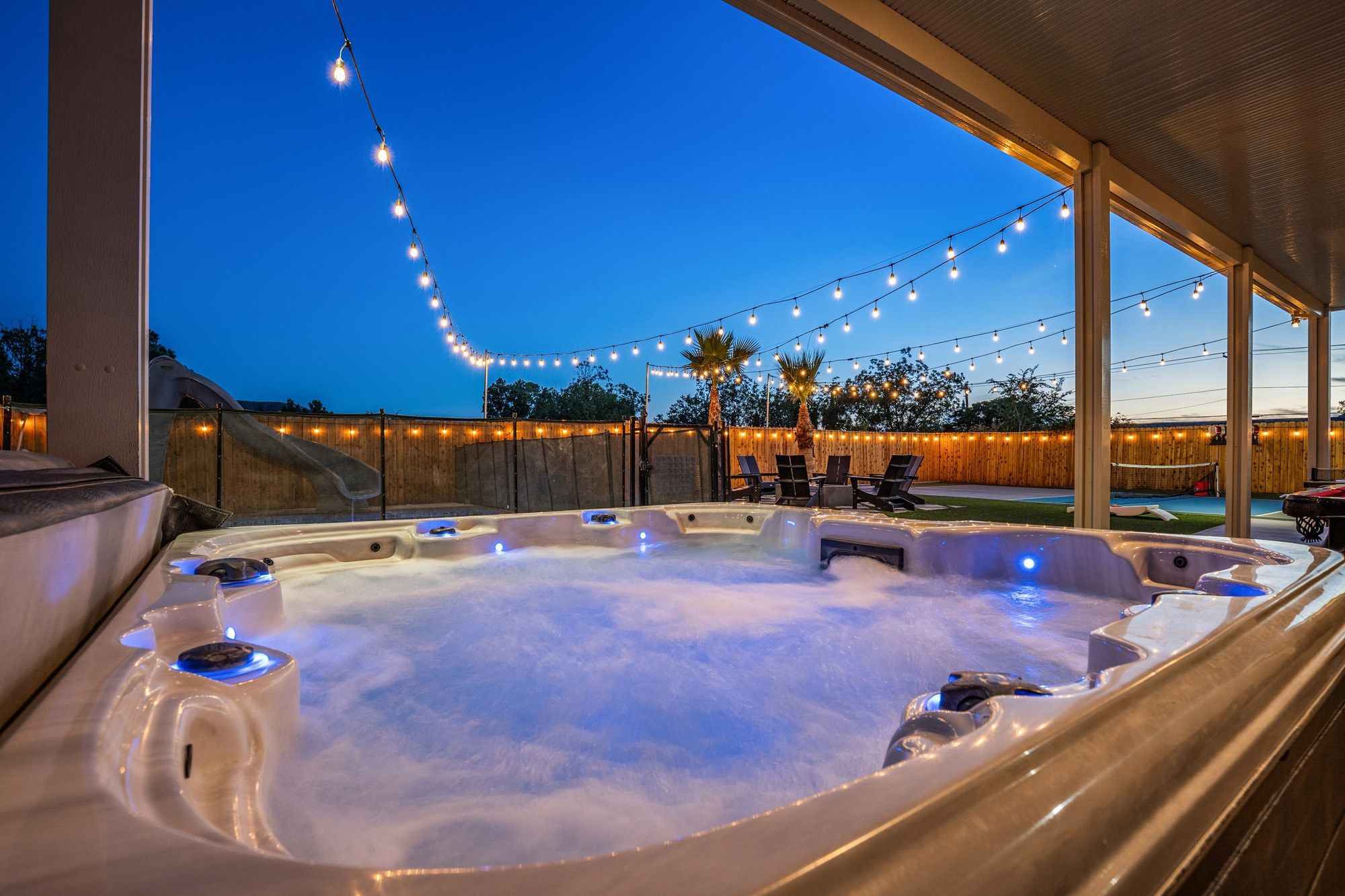 A hot tub with multiple jets, surrounded by a wooden deck and string lights.
