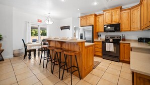 A modern kitchen with wooden cabinets, a stainless steel refrigerator, a microwave, and a large island with bar stools.