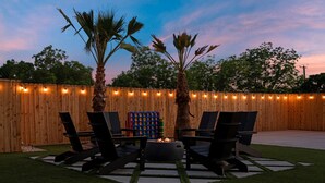 A backyard with a wooden fence, two palm trees, a fire pit, and outdoor seating.