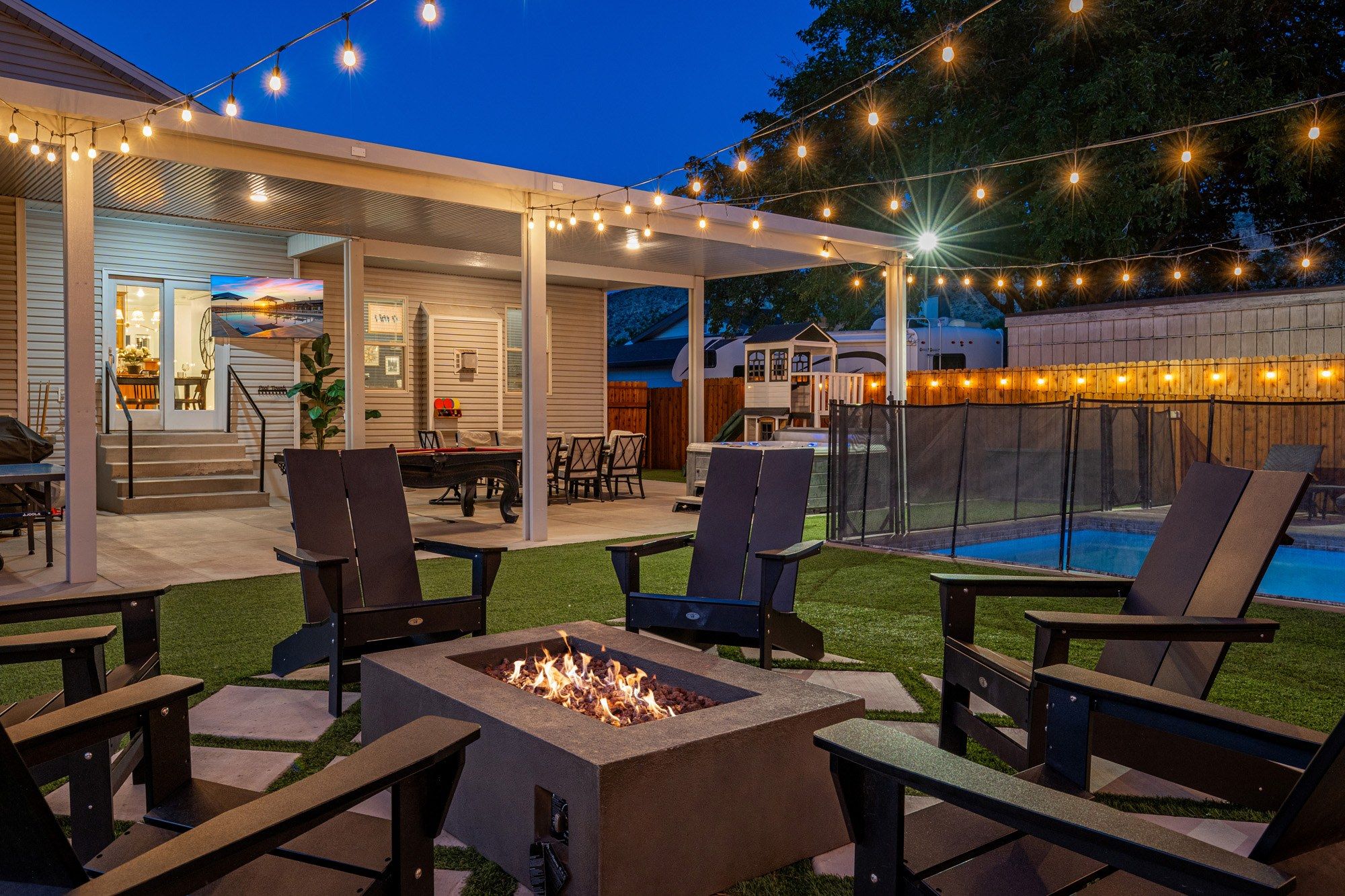 An outdoor patio area with a fire pit, seating, and string lights.