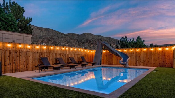 A backyard with a swimming pool, lounge chairs, and a wooden fence.
