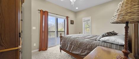 Un dormitorio con cama, ventilador de techo, ventana con cortinas y vista al exterior.