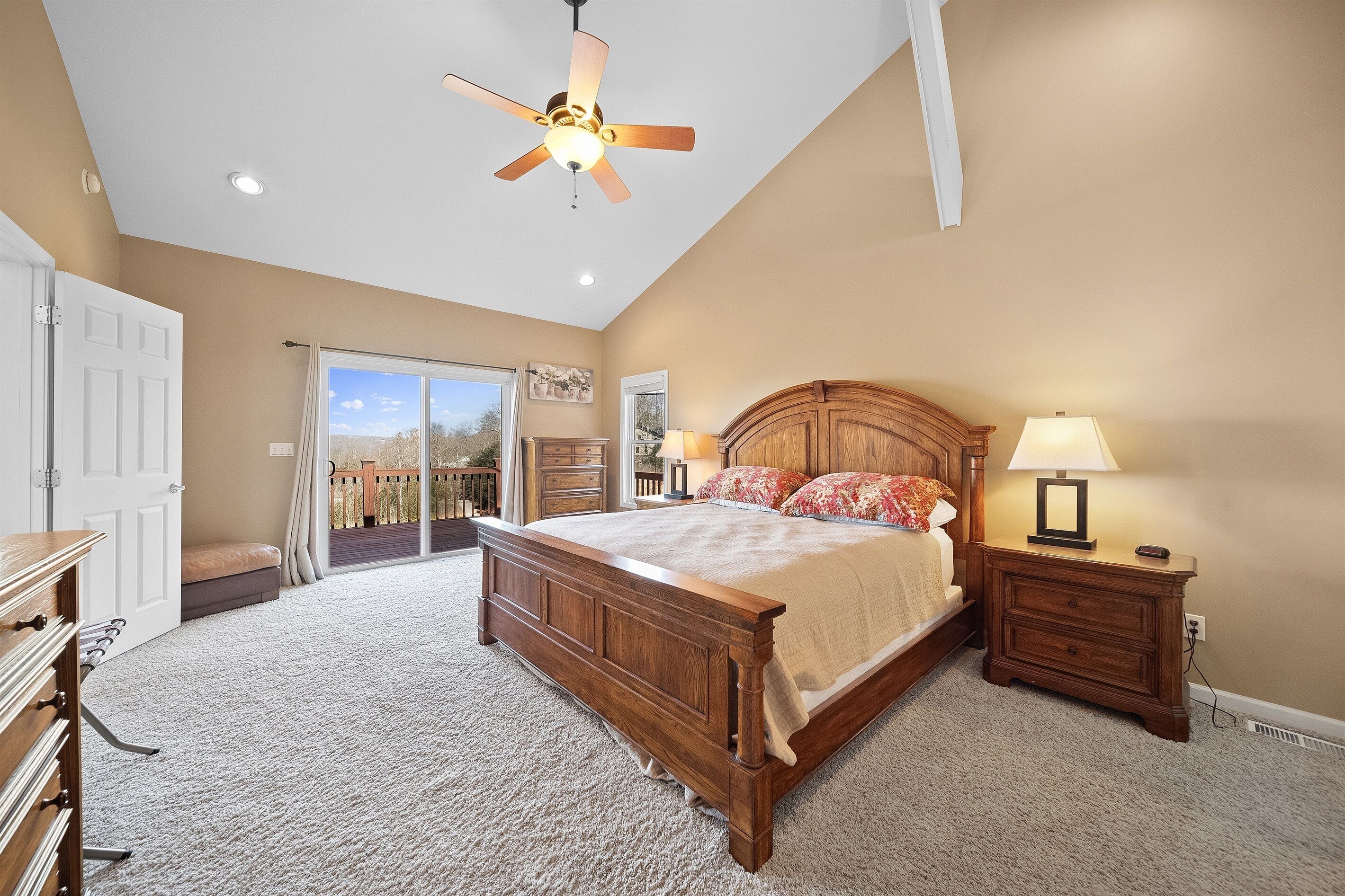 A bedroom with a large bed, a ceiling fan, a nightstand with a lamp, and a view of the outdoors through a sliding door.