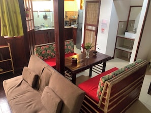 Un salon avec un canapé, une table à manger avec des chaises, un coin cuisine avec un réfrigérateur et une salle de bain avec un miroir.
