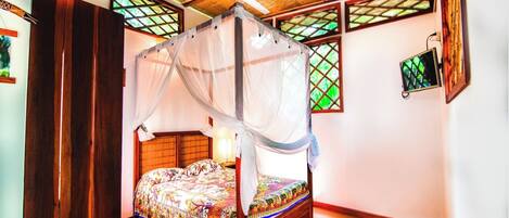 A room with a four-poster bed, a ceiling fan, and a window with a decorative lattice.