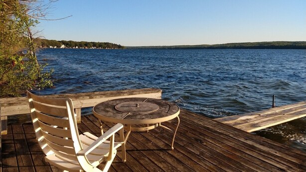Una terraza de madera con una mesa y dos sillas, con vista a un lago.