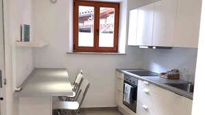 Cocina compacta con gabinetes blancos, horno integrado y ventana con vista al exterior.