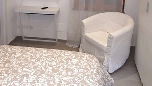 Un dormitorio con cama, televisor montado en un escritorio blanco y una silla.