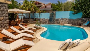 Una piscina con sillones de descanso y un muro de piedra.