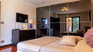 Un dormitorio moderno con una cama grande, un televisor, un aparador y un espejo.