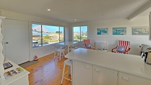 A bright kitchen with a large window, white cabinets, and a dining area with striped chairs. - Kalimna - 360 degree ocean and marina views! (Robe)