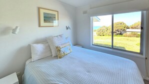 A bedroom with a large bed, a framed picture on the wall, and a window with a view of the outdoors. - Kalimna - 360 degree ocean and marina views! (Robe)