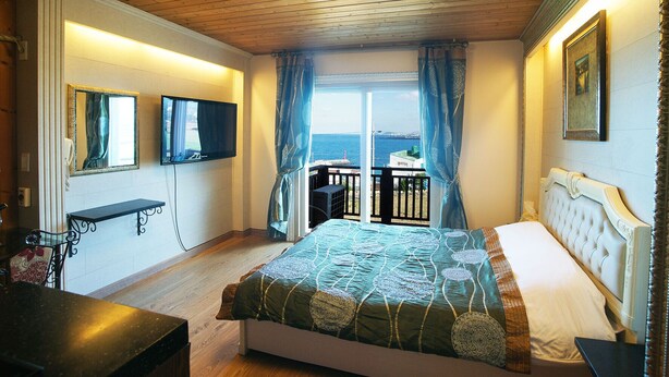 Une chambre avec un lit, une télévision, un balcon donnant sur la mer et un plafond en bois.