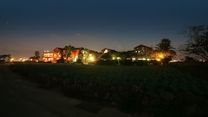 Une rangée de maisons illuminées d’une lumière chaleureuse, un mur de pierre au premier plan et un ciel nocturne dégagé.