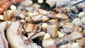 Gros plan sur différentes sortes de viandes en train de griller, notamment des saucisses et du porc.