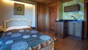 Une chambre avec un lit, une armoire en bois, un petit coin cuisine et un tableau encadré au mur.