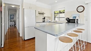 Une cuisine moderne avec des meubles blancs, un grand îlot central doté de tabourets, un four à micro-ondes et une horloge murale.