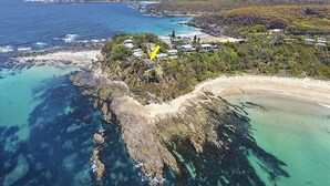 Vue aérienne d’une propriété située sur la côte, avec une plage, un littoral rocheux et quelques bâtiments dispersés.