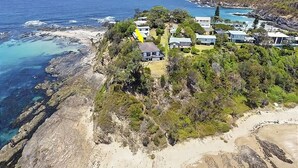 Vue aérienne d’une propriété située sur la côte, avec des maisons, une plage et des falaises rocheuses.