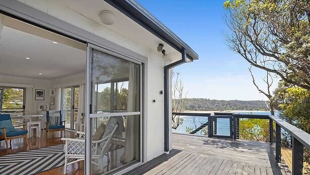 Une maison moderne dotée d’une terrasse, de grandes portes vitrées et offrant une vue sur l’eau.